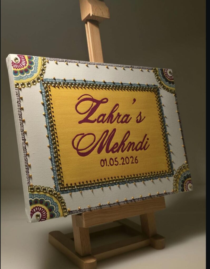 Hand-painted yellow mehndi celebration sign with decorative borders on a wooden easel